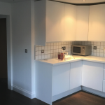 Modern kitchen with white cabinets, tile backsplash, and a microwave on a dark wood floor